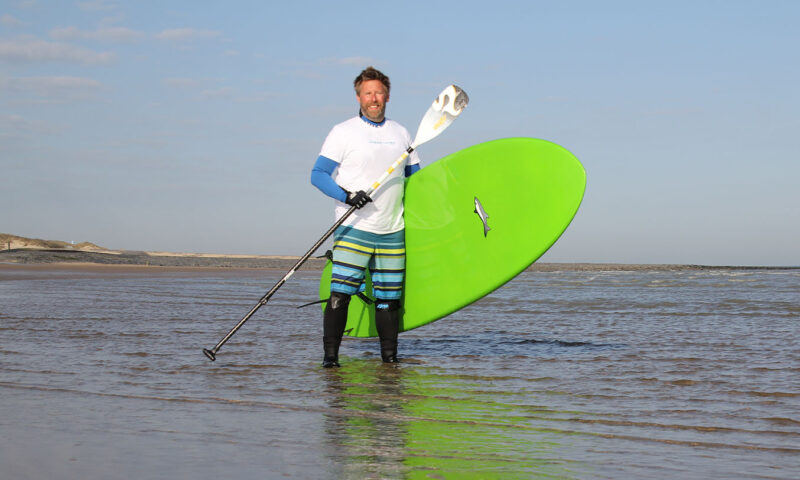 Lars Thierling steht mit einem Surfbrett und Paddel im Wasser