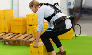 Eine Frau trägt ein Exoskelett, um beim Hochheben einer beschwerten Postbox unterstützt zu werden